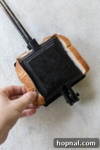 Cast iron pie maker with two buttered bread slices and a generous apple pie filling in between