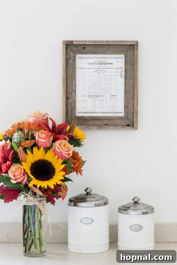 Stylish Printable Kitchen Conversion Guide 3 A beautifully framed kitchen conversion chart, adorned with vibrant flowers, positioned perfectly in a modern kitchen setting.