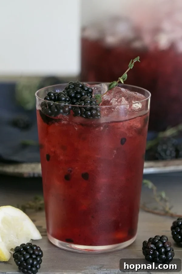 Refreshing Blackberry Thyme Punch in a large glass dispenser, garnished with fresh blackberries and thyme sprigs, perfect for a party.