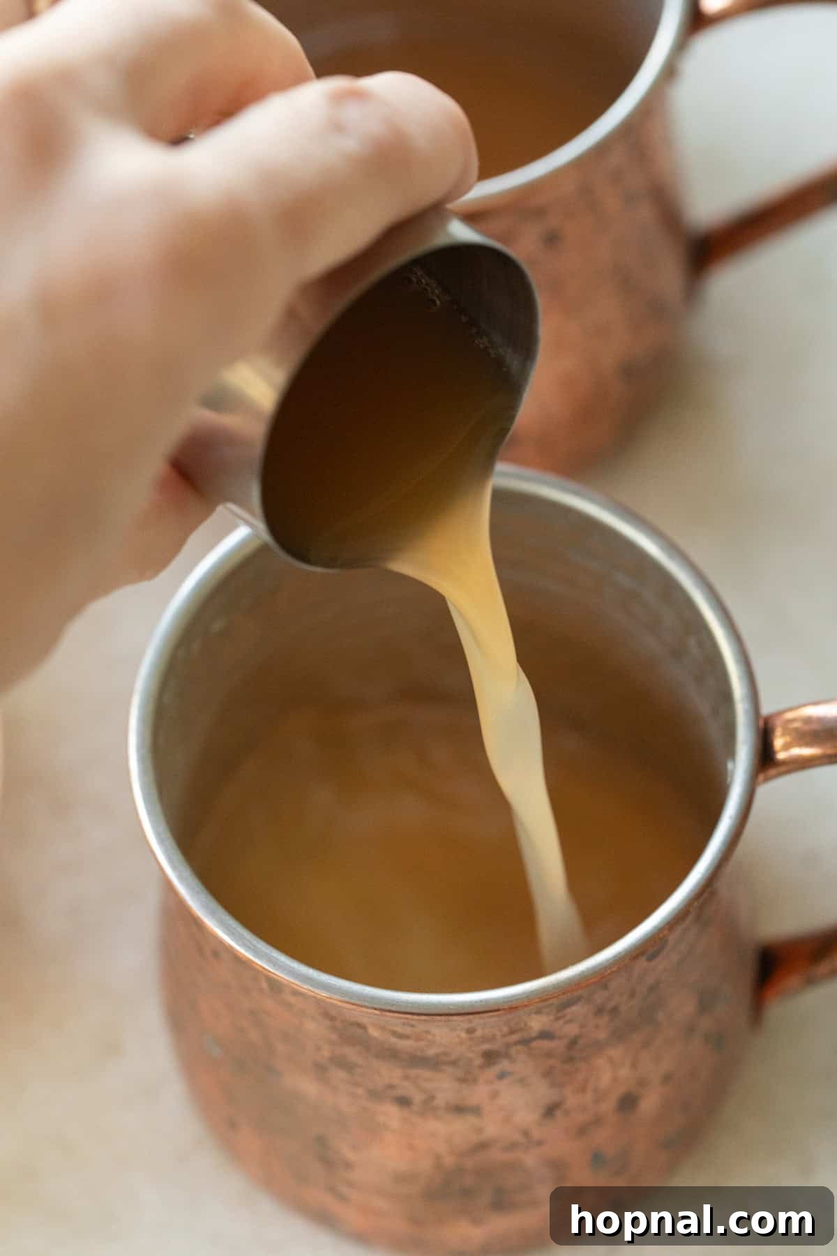 Spiced Apple Cider Moscow Mule 4 The moment of pouring crisp apple cider into a frosty copper mug filled with ice, preparing an Apple Cider Moscow Mule with elegant precision.