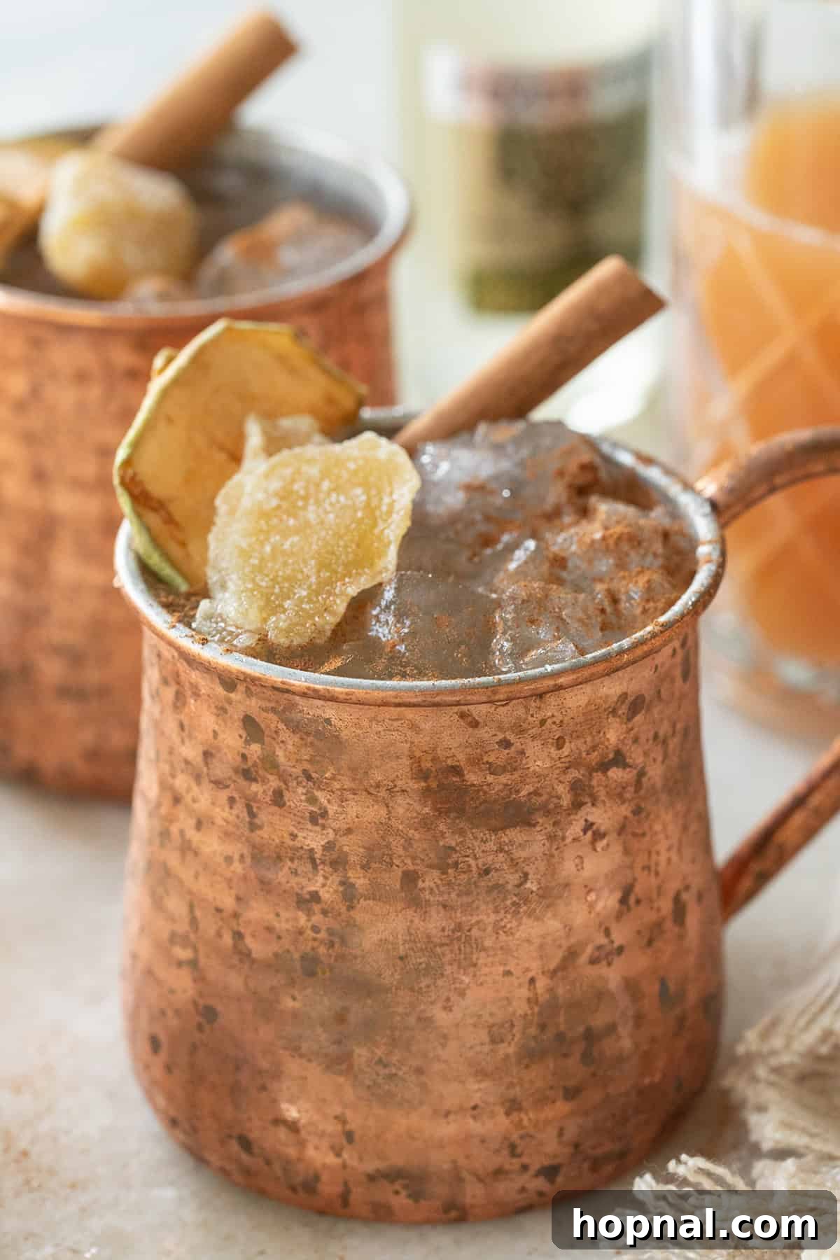 Spiced Apple Cider Moscow Mule 5 A perfectly crafted Apple Cider Moscow Mule in a frosty copper mug, adorned with a vibrant slice of candied ginger and a fragrant cinnamon stick, presented beautifully on a dark surface.