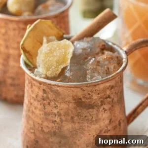 A close-up of a Moscow mule cocktail recipe featuring apple cider and ginger, served in a traditional copper mug with ice.