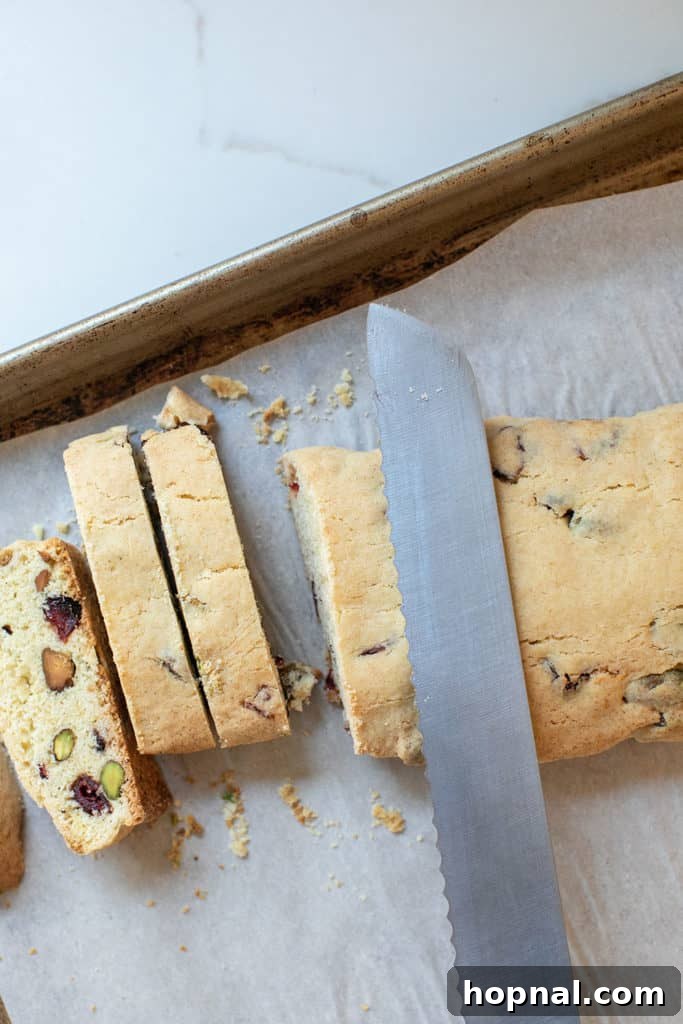 Jeweled Cranberry Pistachio Biscotti 11 A serrated knife slicing the baked biscotti log into individual cookies.