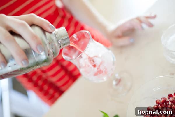 A vibrant Strawberry Pomegranate Mojito being poured into a tall glass, garnished with fresh fruit and mint.
