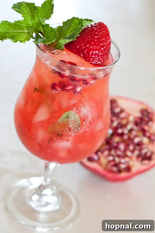 A close-up side view of a freshly made Strawberry Pomegranate Mojito in a tall, condensation-beaded glass.