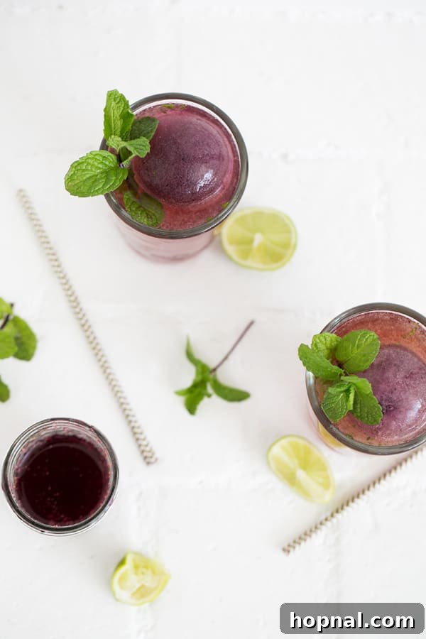 Close-up of a large, round blueberry ice cube melting in a mojito glass, adding subtle color and flavor.