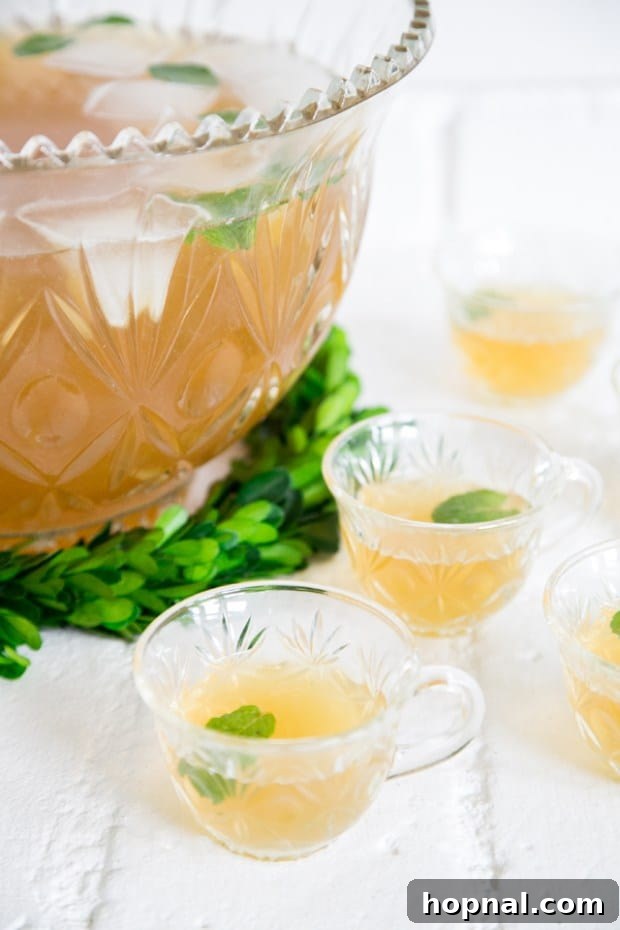 A large, ornate glass punch bowl filled with a vibrant green whiskey punch, garnished generously with fresh lemon slices and aromatic mint leaves, creating a festive centerpiece for a St. Patrick's Day celebration.