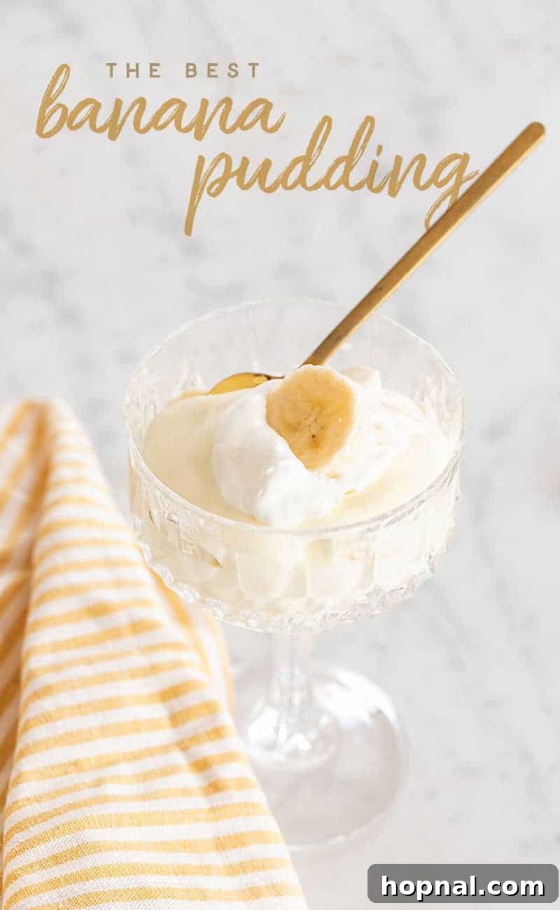 Heavenly Banana Pudding 2 A serving of creamy banana pudding in a clear glass, topped with homemade whipped cream and a banana slice, with a gold spoon and a striped yellow towel beside it.