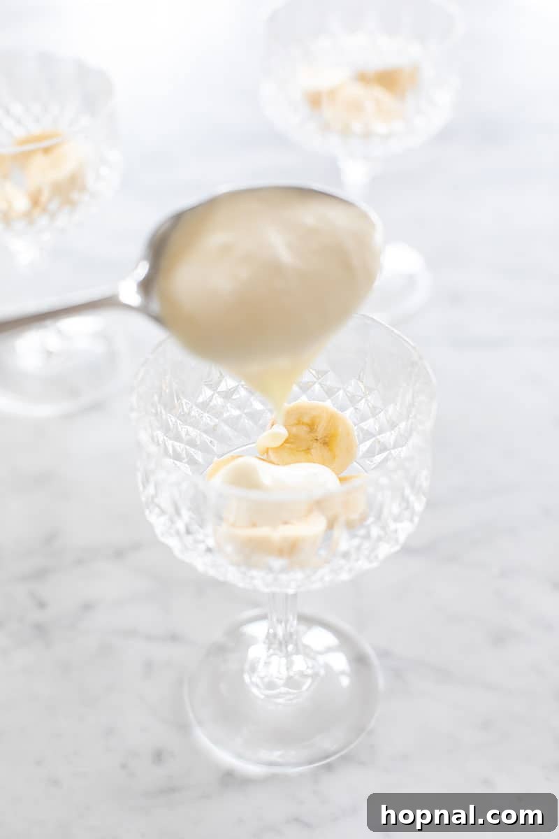 Heavenly Banana Pudding 11 A scoop of banana pudding being carefully placed into a small, clear glass, forming the first layer over the bananas.
