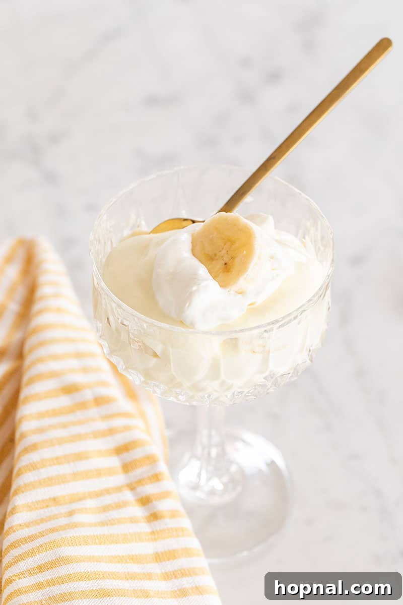 Heavenly Banana Pudding 14 A beautifully presented individual banana pudding with whipped cream and a banana slice, resting on a yellow striped towel beside a gold spoon.