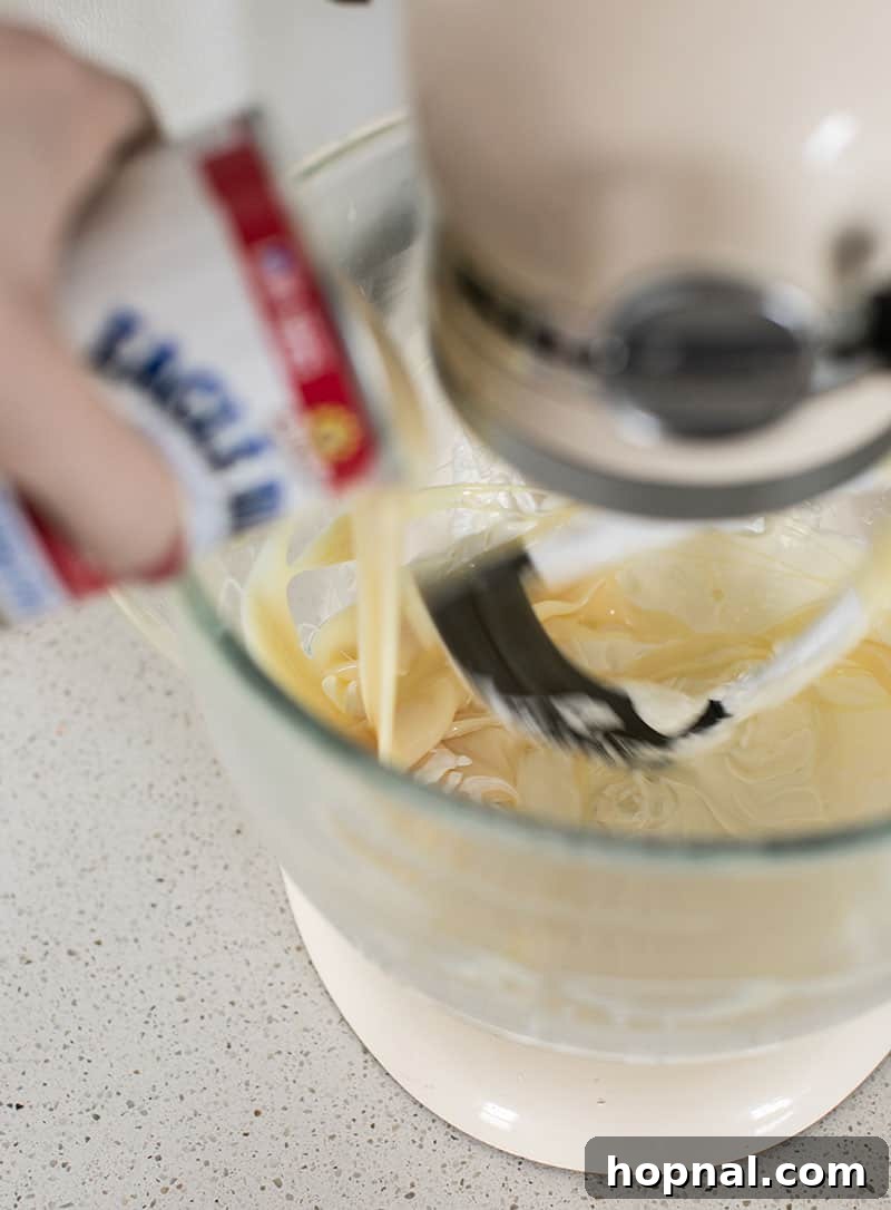 Heavenly Banana Pudding 8 Sweetened condensed milk being poured into a bowl with cream cheese in an electric mixer, indicating the start of combining the pudding ingredients.