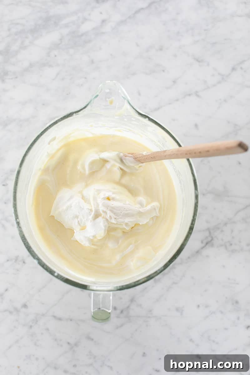 Heavenly Banana Pudding 9 Homemade whipped cream being gently folded into the creamy banana pudding mixture in a large bowl, demonstrating the blending process.