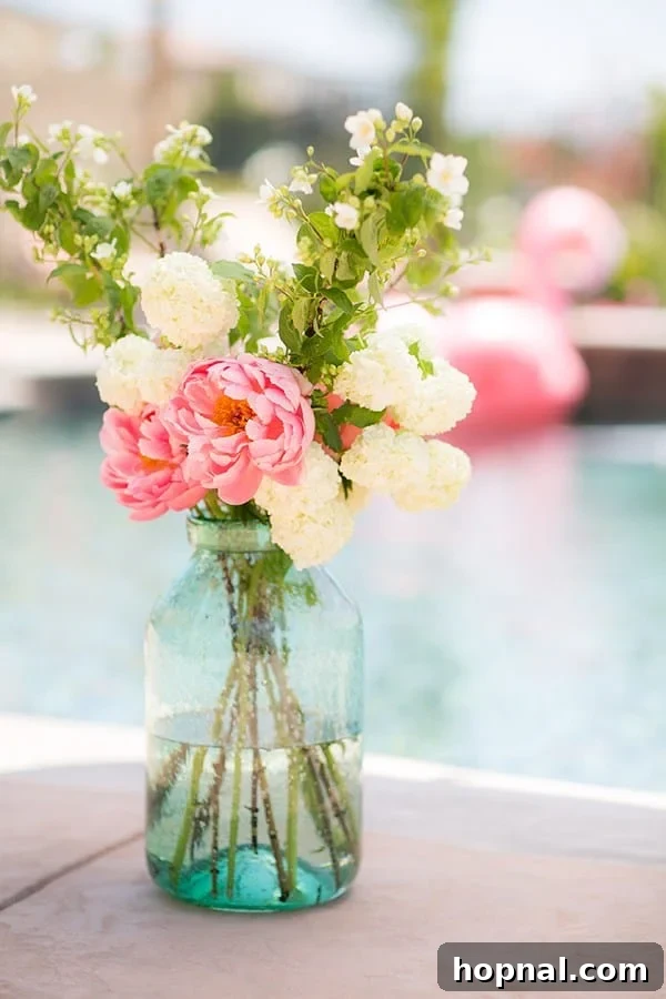 Large green glass vase with a beautiful flower arrangement next to a flamingo pool party setup