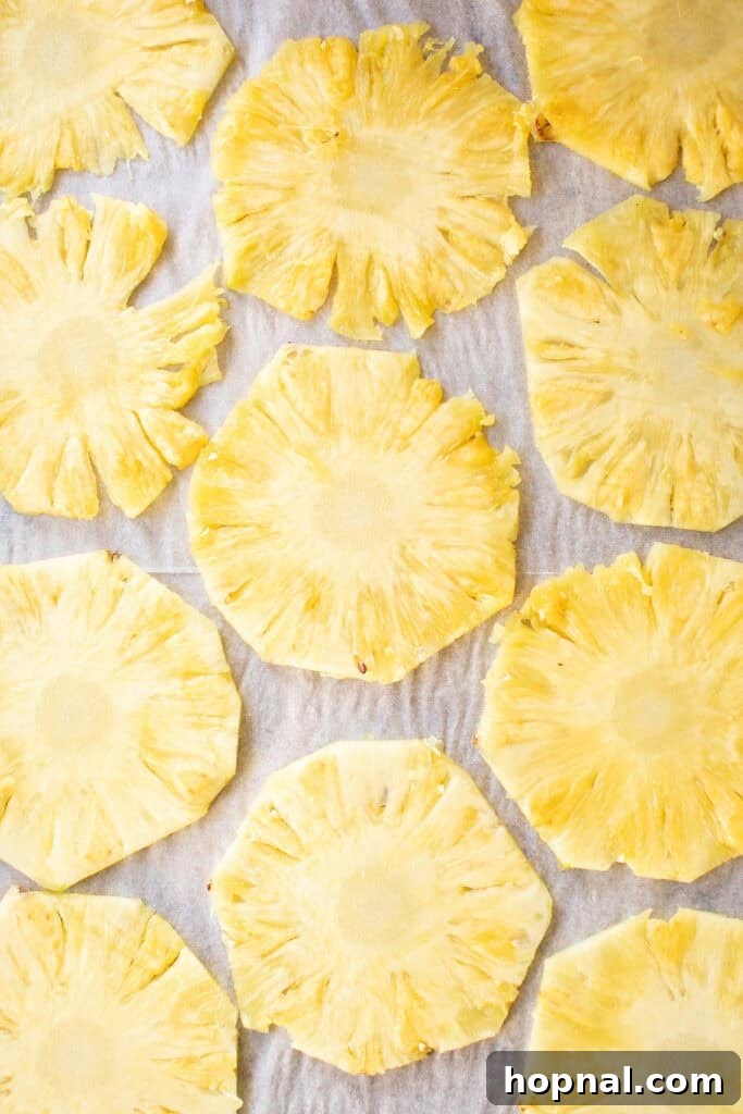 Thin pineapple slices meticulously placed in a single layer on parchment paper, ready for the oven.