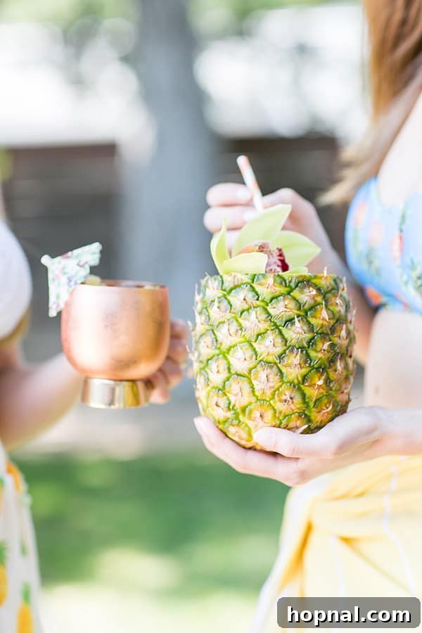 Two cheerful girls holding a pineapple mojito and a pineapple Moscow Mule, showcasing their tropical drinks.