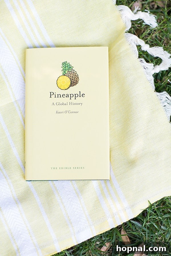 A pineapple history book resting on a bright yellow towel, set against a tropical backdrop.
