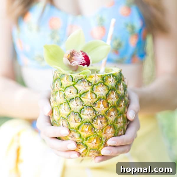 A close-up of a girl holding a fresh pineapple cocktail, showcasing the vibrant colors and garnishes.