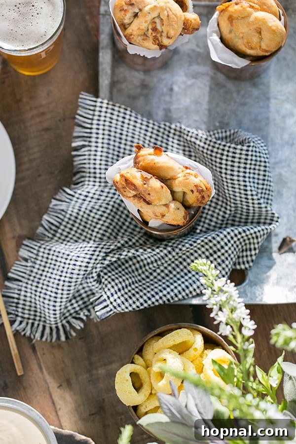 Close-up shot of golden-brown bacon and cheese pretzels artfully arranged on a serving platter, accompanied by a neatly folded napkin and a refreshing glass of beer, highlighting their appealing texture and warmth.