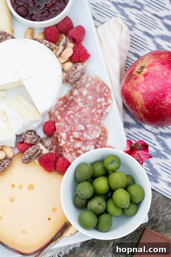 A beautifully arranged cheese board with various cheeses, crackers, and fruits, set up on a campfire grate for Thanksgiving camping.