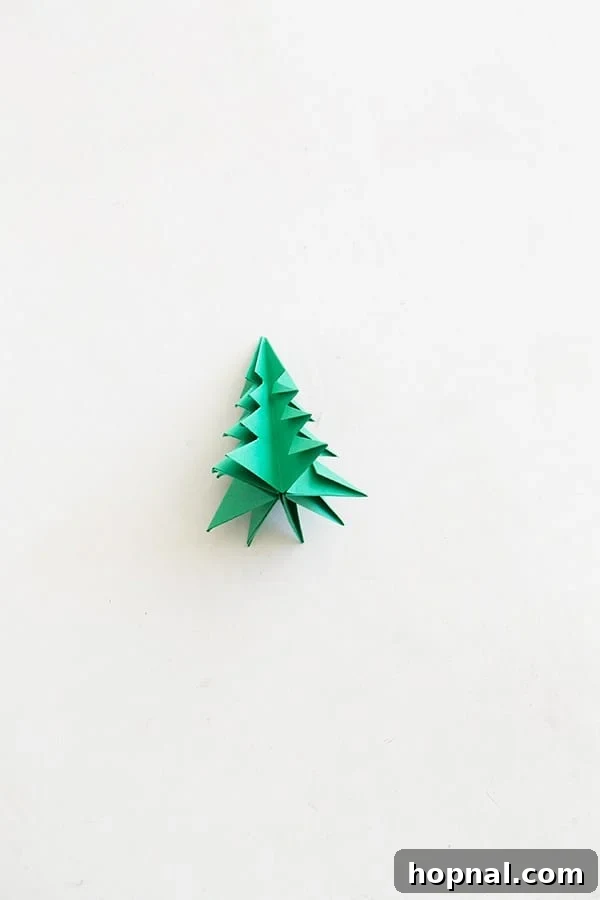 One green paper origami tree on a table. - Example of a finished DIY origami Christmas tree.