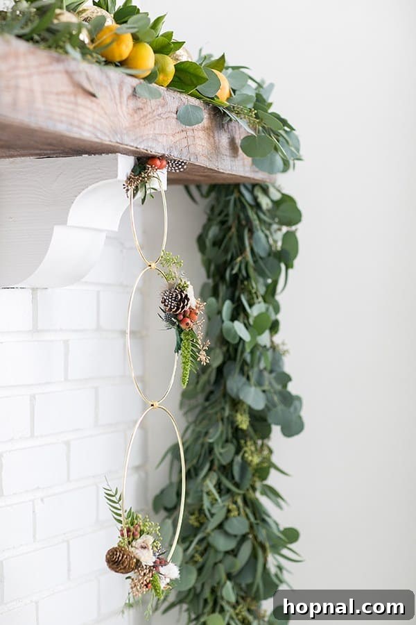 A close-up of a modern Christmas wreath featuring multiple gold metal rings elegantly adorned with fresh green foliage, delicate dried flowers, and natural pinecones, showcasing its contemporary design.