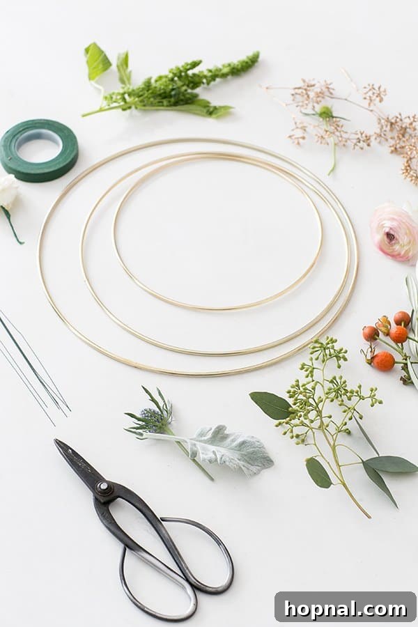 Essential supplies laid out for crafting a modern Christmas wreath: gold metal rings of various sizes, rolls of floral tape, a selection of fresh and dried flowers, and spools of floral wire.