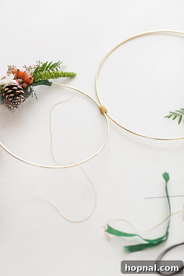 Hands carefully connecting two gold metal rings together using floral wire and tape, demonstrating a key step in assembling a multi-hoop modern Christmas wreath.
