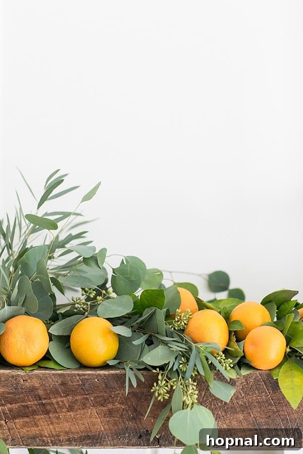 A beautifully decorated Christmas mantel featuring a lush green eucalyptus garland intertwined with bright orange tangerines and subtle gold ornaments, creating a fresh and modern holiday display.