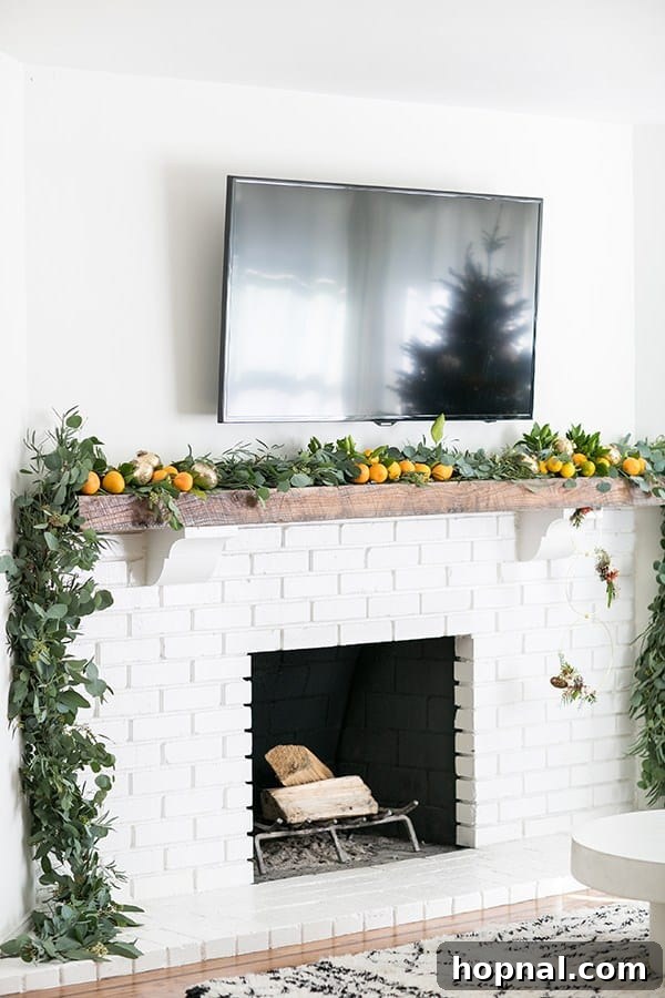 A cozy living room scene with a white fireplace and a TV mounted above, beautifully decorated with a modern eucalyptus garland featuring fresh oranges and gold accents, enhancing the festive atmosphere.