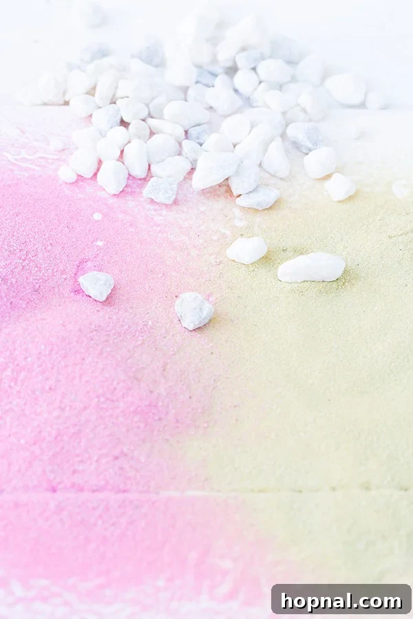 Close-up of a terrarium showing carefully layered pink and gold sand, topped with white rocks, awaiting an air plant.