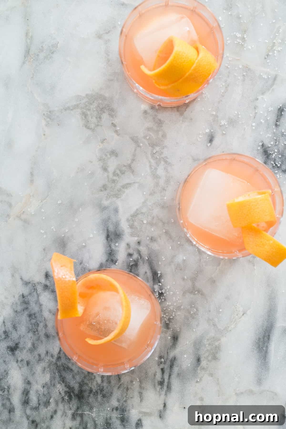 Italian Paloma Spritz 3 Paloma cocktail in a glass with ice and a grapefruit wedge on a white marble table with a dark background.