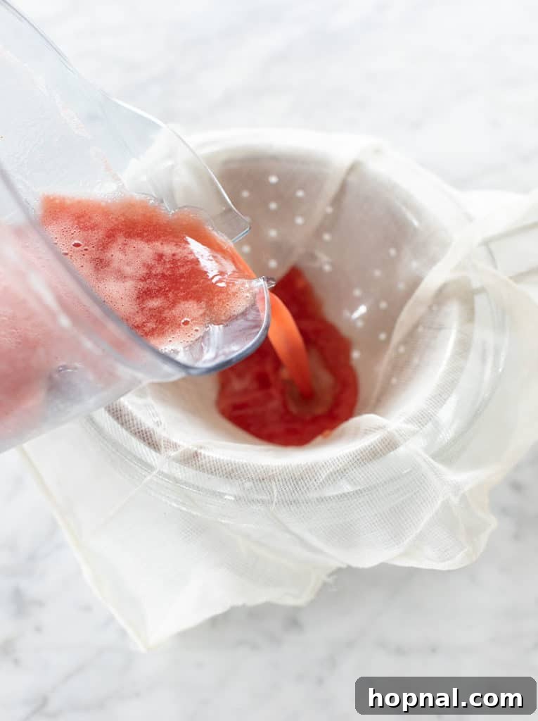 Cool Watermelon Quencher 6 Blended watermelon juice being poured through a fine mesh sieve lined with cheesecloth into a large bowl.
