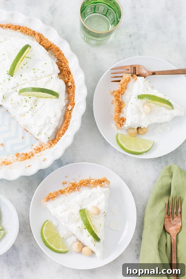 Zesty Island Dream Pie 4 A perfectly sliced piece of coconut key lime pie, showing its distinct layers of crust, creamy filling, and fluffy whipped topping, served on a marble table.