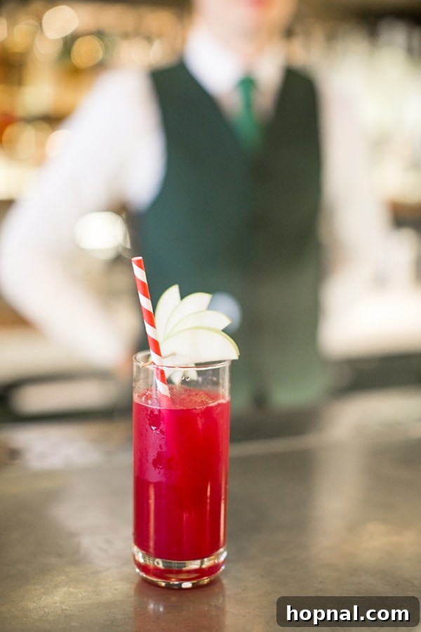 A vibrant red cocktail garnished with a pear slice