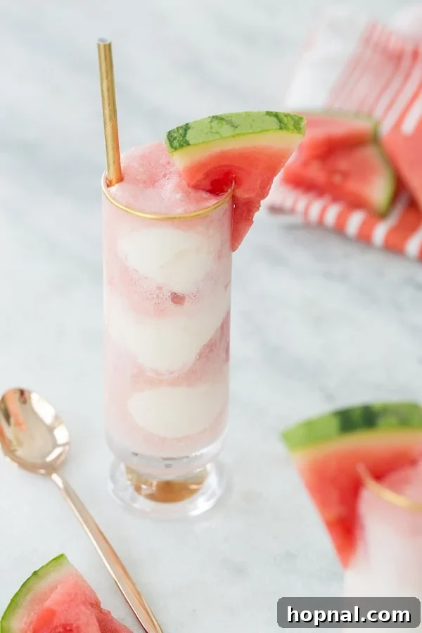 Two glasses of watermelon soda floats with watermelon slices on a rustic wooden table, viewed from the side, highlighting the vibrant red and white layers.