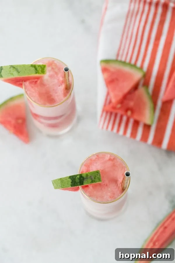 Overhead shot of two watermelon soda floats in tall glasses, garnished with watermelon wedges, on a light-colored surface.