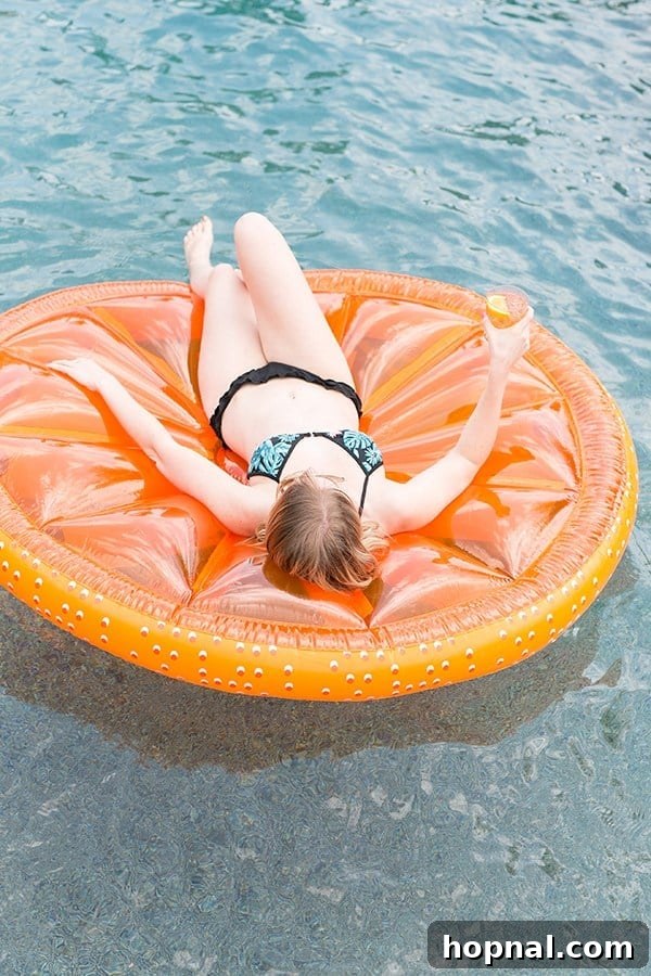 Girl in bathing suit floating on an orange slice in a pool.