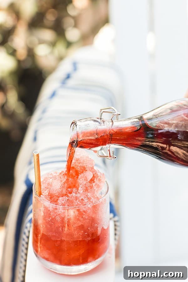 Stars Stripes and Spiked Slushies 7 A hand gracefully pouring vibrant strawberry syrup into a glass brimming with perfectly shaved ice, showcasing the crucial step in creating a refreshing frozen treat.