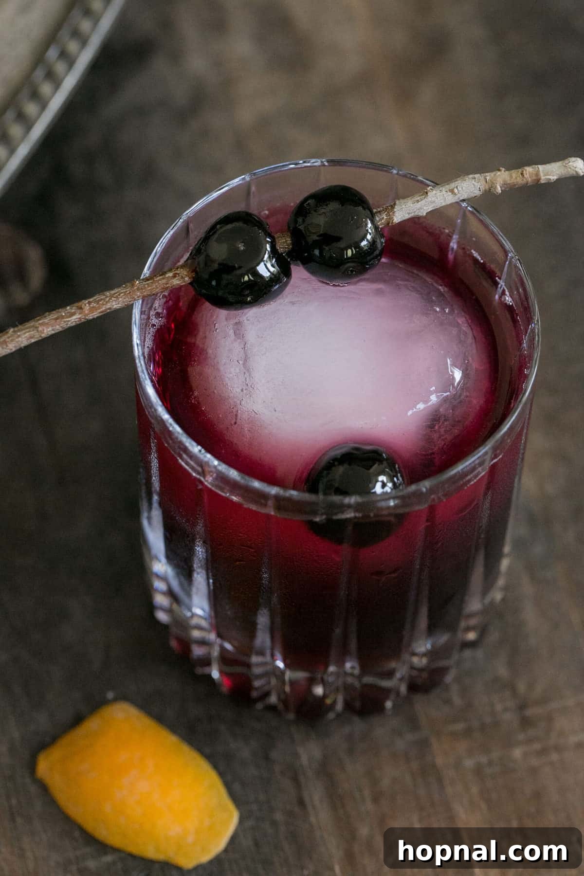 Crimson Moon Manhattan 4 Close-up of a red cocktail with a large ice cube and maraschino cherry garnish