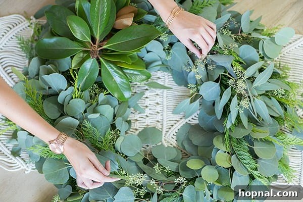 Greenery and Good Times Wreath Party 12 Close-up of hands delicately assembling a holiday wreath, adding festive elements and greenery