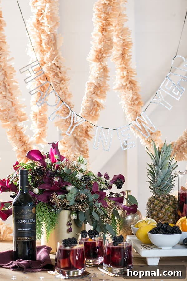 Glasses of red sangria with fresh fruit, a bottle of red wine, and a 'Happy New Year' sign draped with a festive garland, setting a vibrant New Year's Eve party atmosphere.