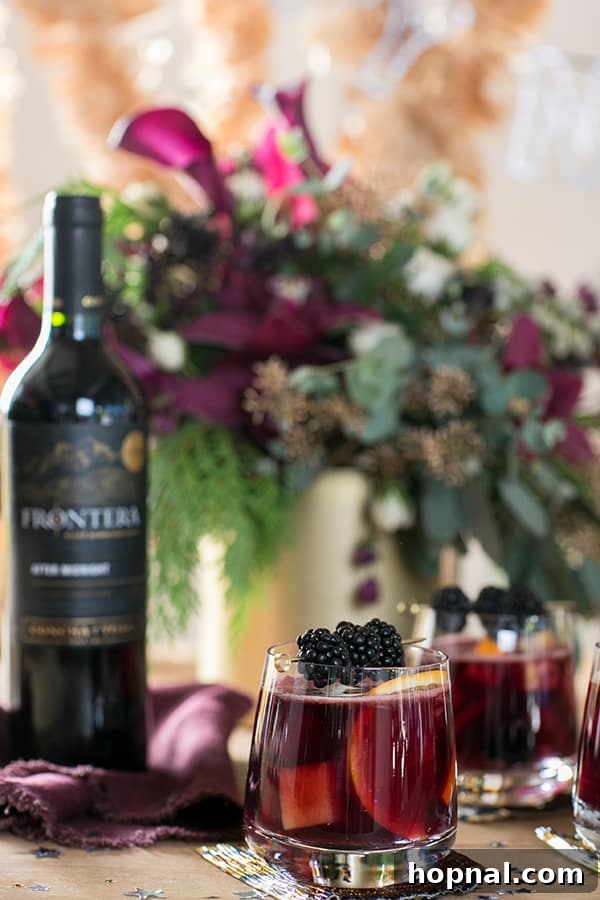 A close-up of a glass of red sangria garnished with blackberries, placed next to a bottle of red wine on a festive table, highlighting the rich colors and flavors.