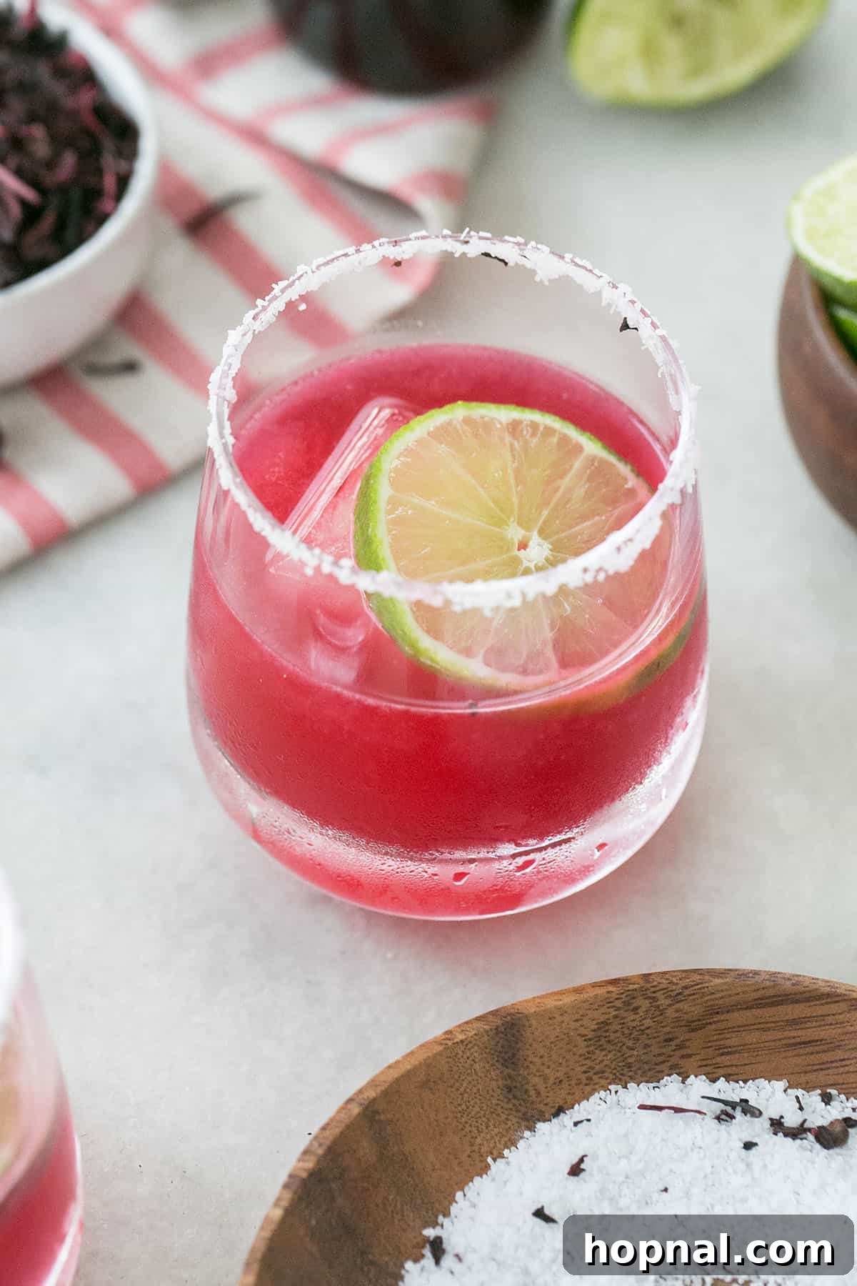 Vibrant pink hibiscus margarita with a salted rim and a fresh lime wheel garnish, presented on a light background.