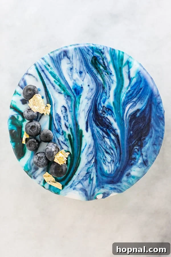 A close-up of a marble drip cake embellished with fresh blueberries and delicate gold leaf, highlighting its elegant finish.