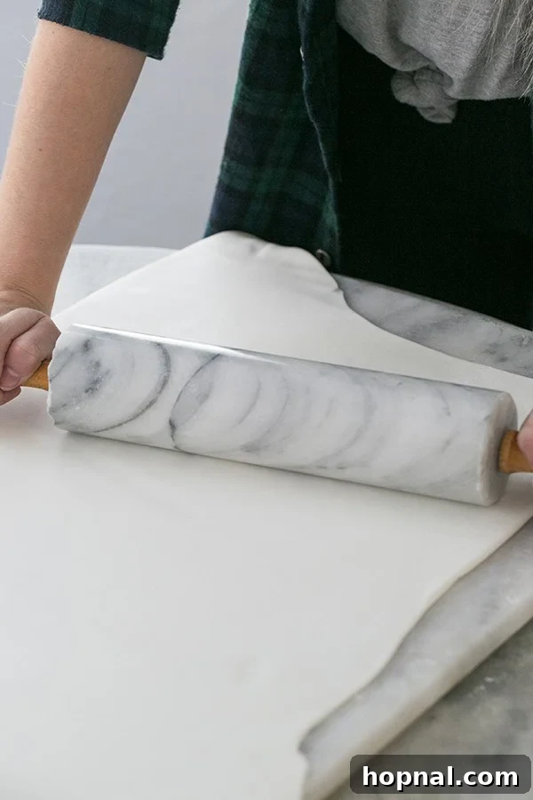 A baker's hands skillfully rolling out white fondant on a clean surface.