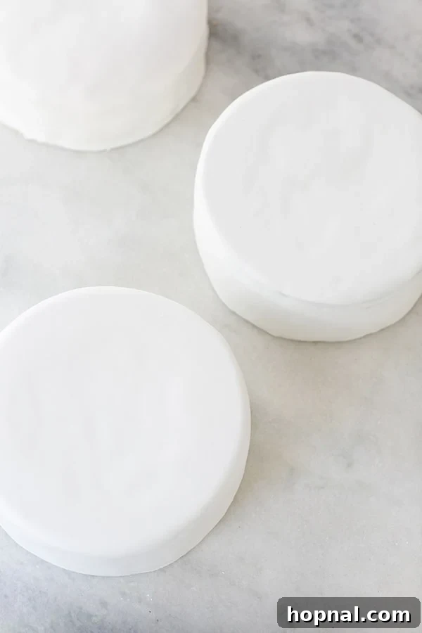 Several cakes neatly covered in smooth white fondant, stacked or arranged, awaiting the drip decoration.
