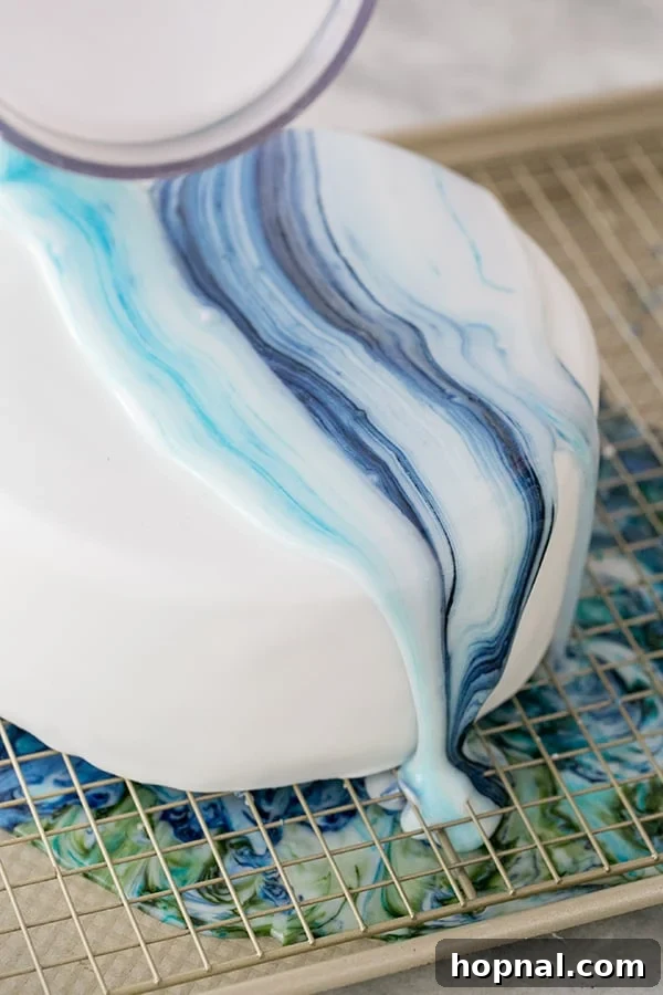 A baker carefully pouring marbled frosting over a fondant-covered cake, illustrating the drip effect.