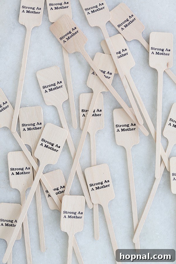 A close-up of custom wooden stir sticks, each elegantly engraved with the heartfelt message 'strong as a mother,' laid on a natural wooden surface.