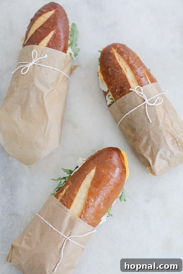Gourmet sandwiches on pretzel bread, beautifully wrapped in brown paper and tied with twine for a rustic and appealing presentation.