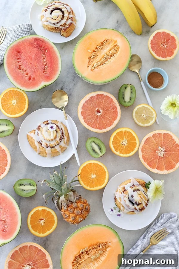 Effortless Brunch Bliss 2 Vibrantly sliced tropical fruit artfully arranged on a table alongside warm cinnamon rolls, creating an inviting brunch spread.